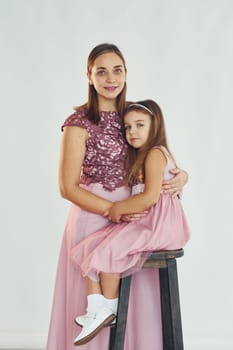 Woman in dress standing with her daughter in the studio with white background.