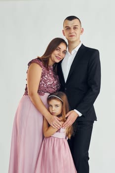 Happy couple with little daughter is standing in the studio.