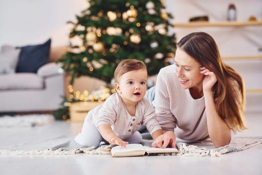 Reading book together. Mother with her little daughter is indoors at home together.