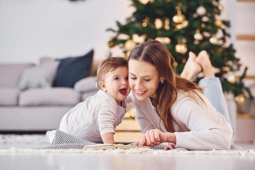 Reading book together. Mother with her little daughter is indoors at home together.