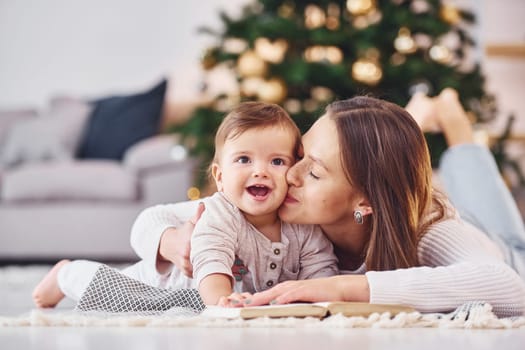 With book that is on the ground. Mother with her little daughter is indoors at home together.