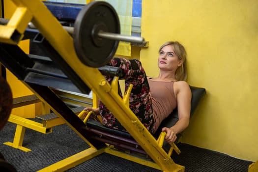 A girl uses an exercise bench available at a gym. The woman is sitting at an angle, facing up and looking at the ceiling. Her legs are up in the air. A wall painted yellow can be seen in the background.