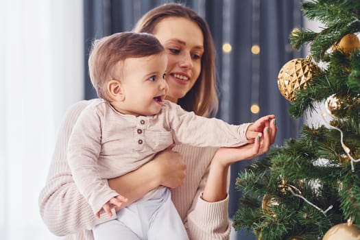 Decorating Christmas tree. Mother with her little daughter is indoors at home together.