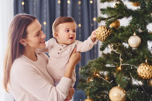 Decorating Christmas tree. Mother with her little daughter is indoors at home together.
