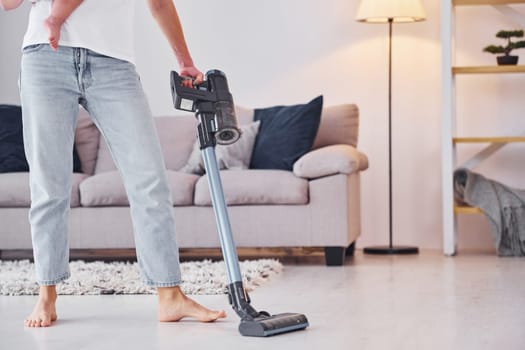 Woman uses vacuum cleaner. Mother with her little daughter is indoors at home together.