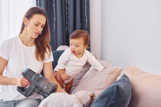 Sitting on the bed with vacuum cleaner part. Mother with her little daughter is indoors at home together.