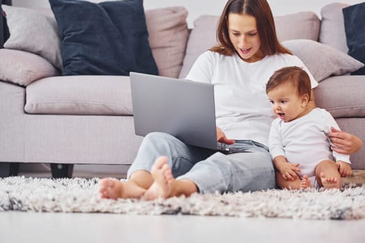 Using laptop. Mother with her little daughter is indoors at home together.