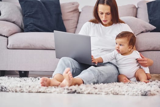 Using laptop. Mother with her little daughter is indoors at home together.