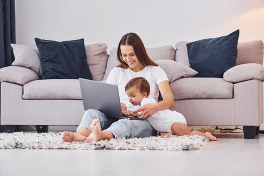 Using laptop. Mother with her little daughter is indoors at home together.