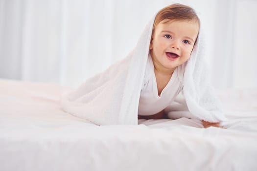 With white towel. Cute little baby is indoors in the domestic room.