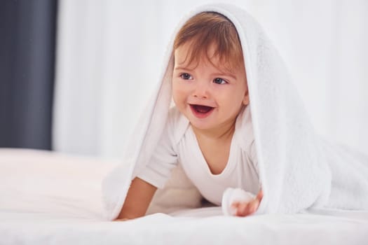 With white towel. Cute little baby is indoors in the domestic room.