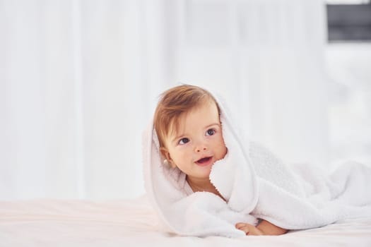 With white towel. Cute little baby is indoors in the domestic room.