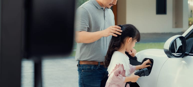 Progressive father and daughter returned from school in electric vehicle that is being charged at home. Electric vehicle driven by renewable clean energy. Home charging station concept for environment