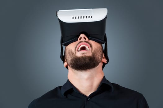 Excited young man using a VR headset glasses and experiencing virtual reality on grey blue background