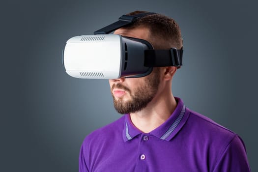 Excited young man using a VR headset glasses and experiencing virtual reality on grey blue background