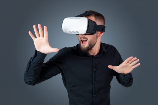 Excited young man using a VR headset glasses and experiencing virtual reality on grey blue background