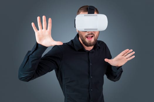 Excited young man using a VR headset glasses and experiencing virtual reality on grey blue background