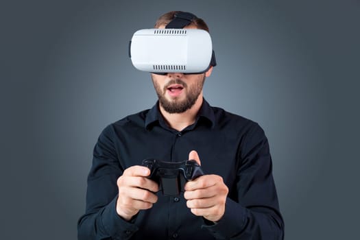 Excited young man using a VR headset glasses and experiencing virtual reality on grey blue background. with a joystick in their hands