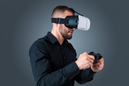 Excited young man using a VR headset glasses and experiencing virtual reality on grey blue background. with a joystick in their hands