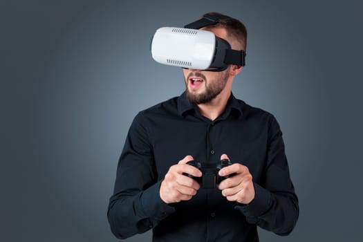 Excited young man using a VR headset glasses and experiencing virtual reality on grey blue background. with a joystick in their hands