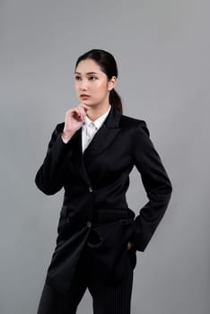 Confident young businesswoman stands on isolated background, posing in formal black suit. Office lady or manager with smart and professional appearance. Enthusiastic