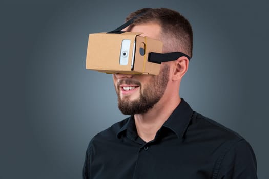 Excited young man using a VR headset glasses and experiencing virtual reality on grey blue background