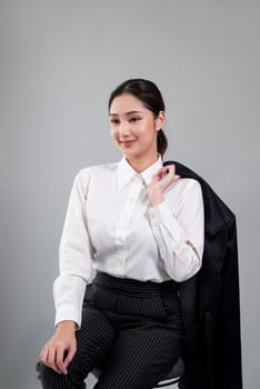 Confident young businesswoman sitting on a chair on isolated background, posing in formal black suit. Successful office lady or manager with smart and professional appearance. Enthusiastic