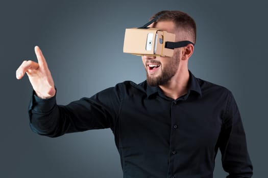 Excited young man using a VR headset glasses and experiencing virtual reality on grey blue background