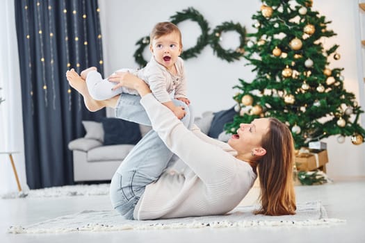 Laying down on the ground and having fun. Mother with her little daughter is indoors at home together.