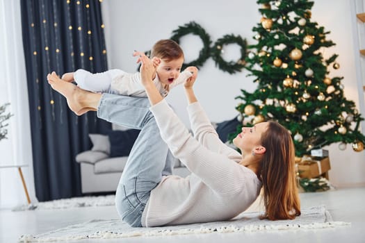 Laying down on the ground and having fun. Mother with her little daughter is indoors at home together.