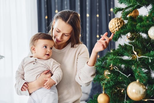 Decorating Christmas tree. Mother with her little daughter is indoors at home together.