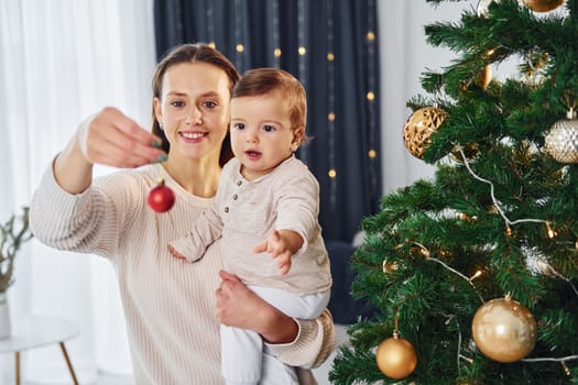 With beautiful tree. Mother with her little daughter is indoors at home together.