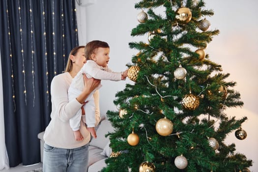 With beautiful tree. Mother with her little daughter is indoors at home together.