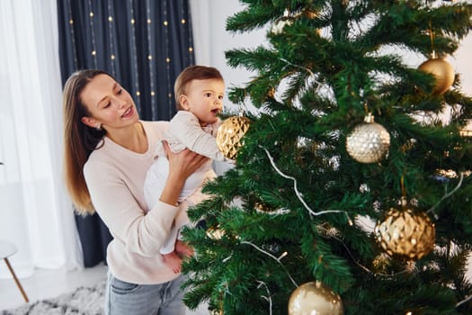 Standing near tree. Mother with her little daughter is indoors at home together.