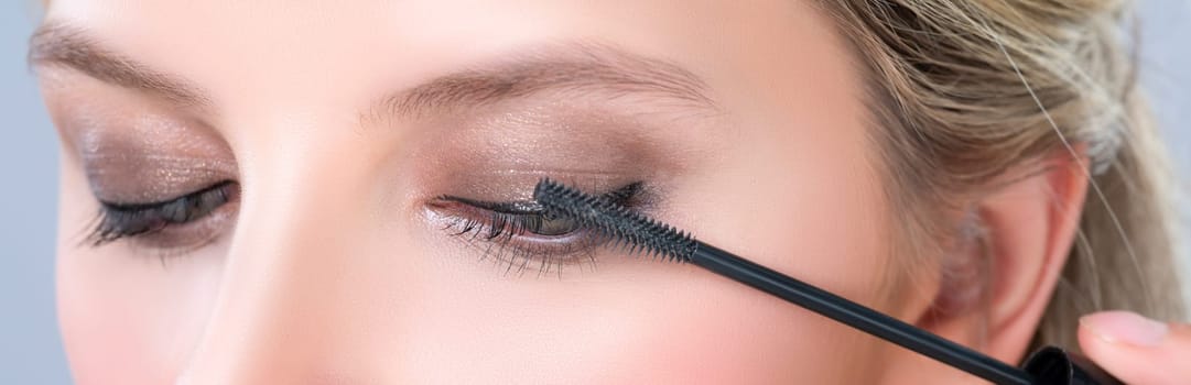 Closeup woman with blond hair putting alluring black mascara with brush in hand on long thick eyelash. Perfect fashionable cosmetic clean facial skin with beautiful eye young woman in high resolution.