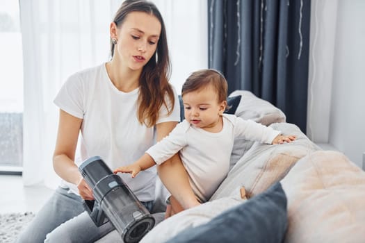 Little part of the vacuum cleaner. Mother with her little daughter is indoors at home together.