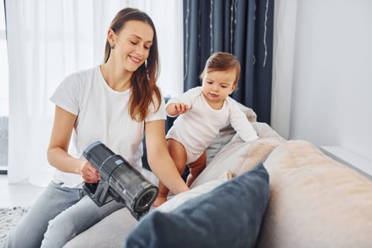 Little part of the vacuum cleaner. Mother with her little daughter is indoors at home together.