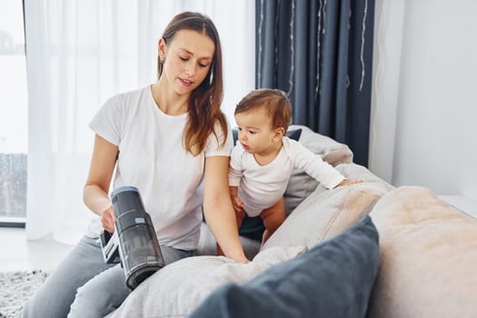 Little part of the vacuum cleaner. Mother with her little daughter is indoors at home together.