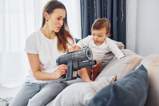Little part of the vacuum cleaner. Mother with her little daughter is indoors at home together.