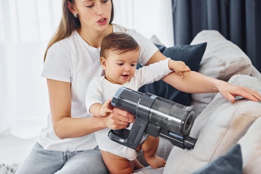 Little part of the vacuum cleaner. Mother with her little daughter is indoors at home together.