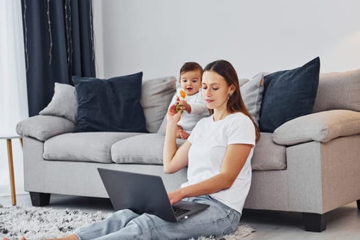 Using laptop. Mother with her little daughter is indoors at home together.