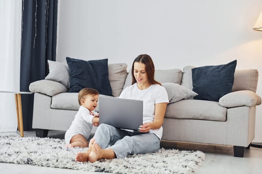 Using laptop. Mother with her little daughter is indoors at home together.