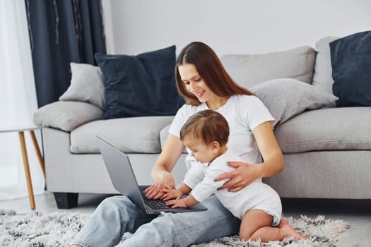 Watching at the laptop. Mother with her little daughter is indoors at home together.