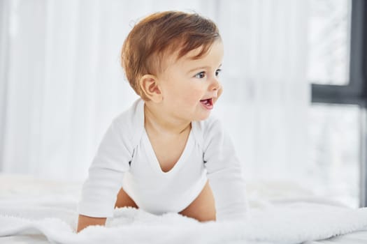 Playing on the bed. Cute little baby is indoors in the domestic room.