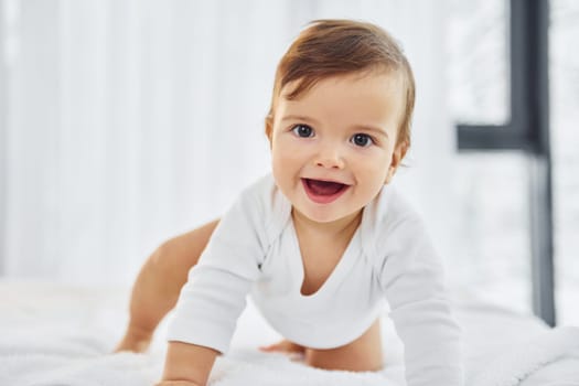 Playing on the bed. Cute little baby is indoors in the domestic room.
