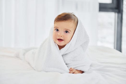 With white towel. Cute little baby is indoors in the domestic room.