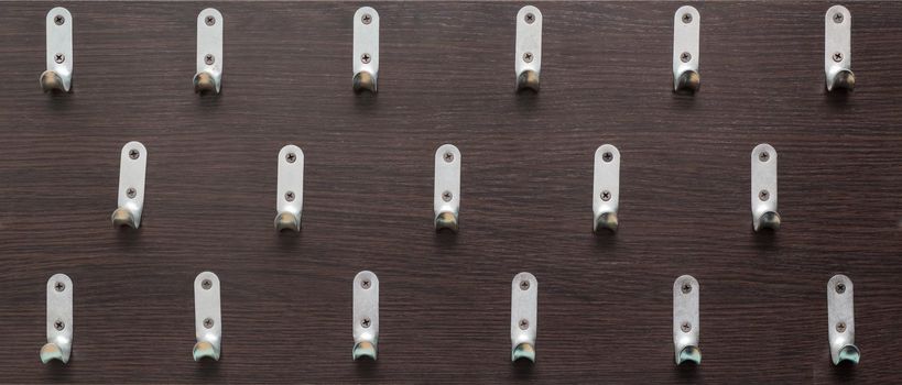 Three rows of metal hooks hang unevenly. Homemade clothes hanger. The hooks are screwed to the board with self-tapping screws.