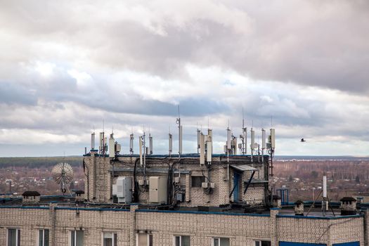 Antennas for cellular transmitters on the roof of a high-rise building. The facade of the house with windows against the background of a gloomy sky. Mobile phone tower next to housing. Radio emission