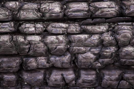 The texture of a black burnt wood surface. Rectangular coals are arranged in a line across the entire surface. Vintage background.