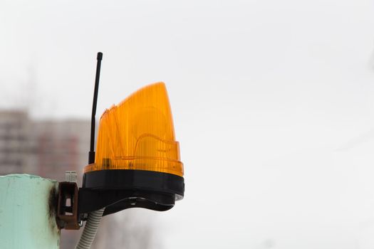 Close-up of a yellow beacon with an antenna for transmitting an alarm. Signal lamp on a metal pole against a gray sky. The concept of industry, construction, health and safety.